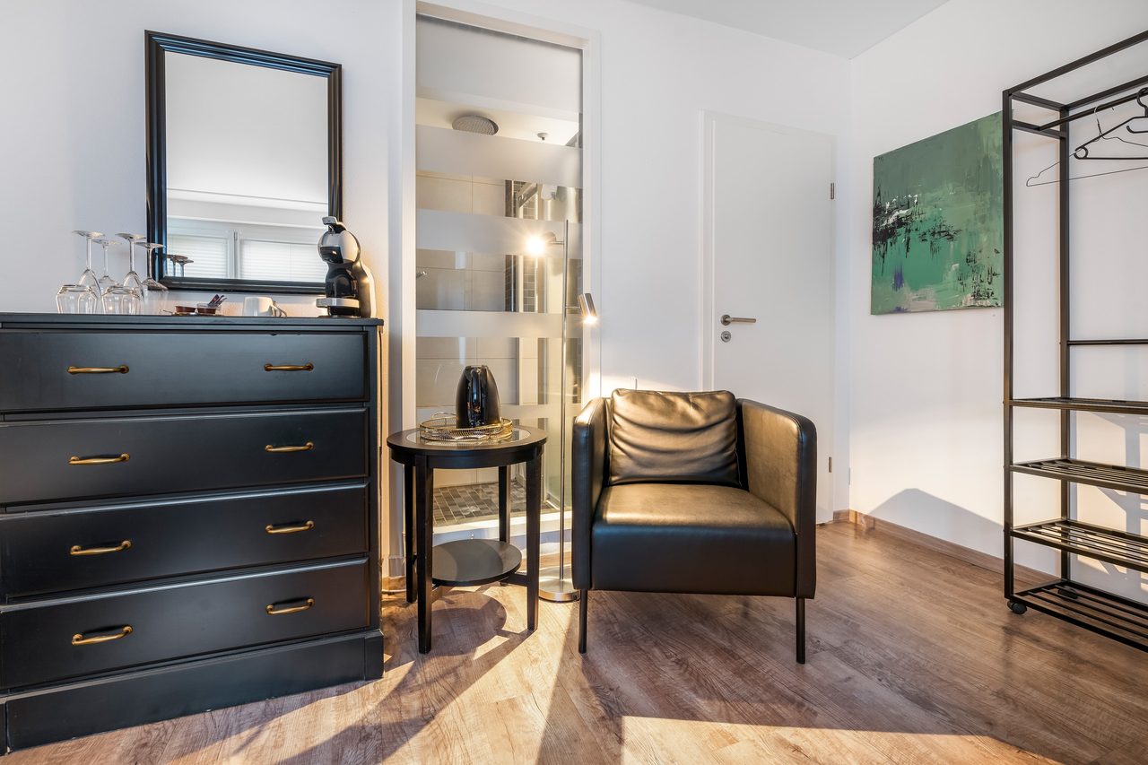 Zimmer mit schwarzer Kommode, Ledersessel und offener Garderobe