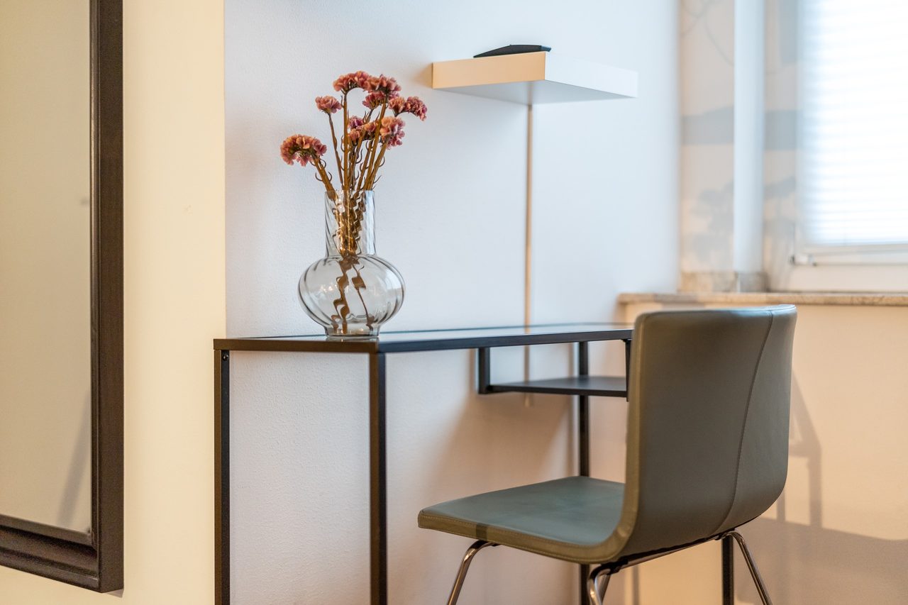 Schreibtisch mit Stuhl und Blumenvase vor dem Fenster