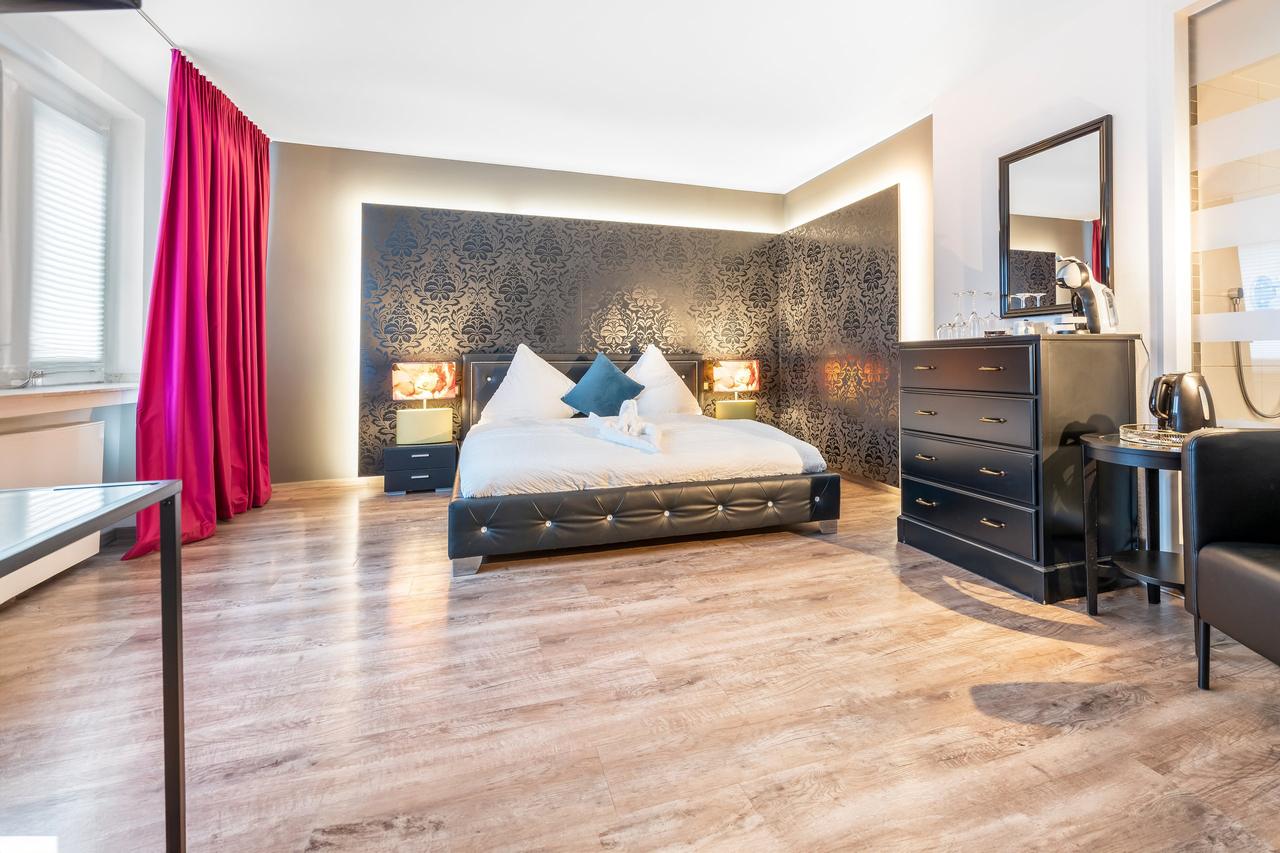 Schlafzimmer mit Doppelbett, schwarzer Kommode und pinkem Vorhang