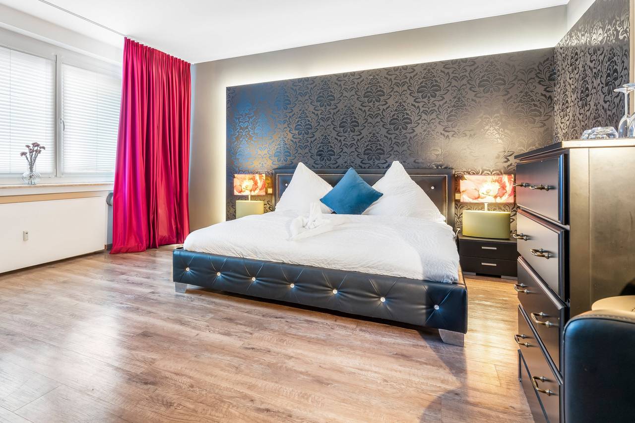 Doppelbett mit blauem Kissen vor dunkler Mustertapete