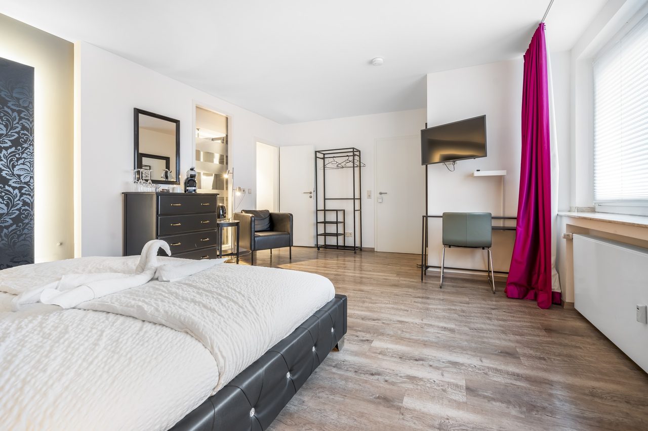 Zimmer mit Bett, Wandfernseher, Schreibtisch und Garderobe