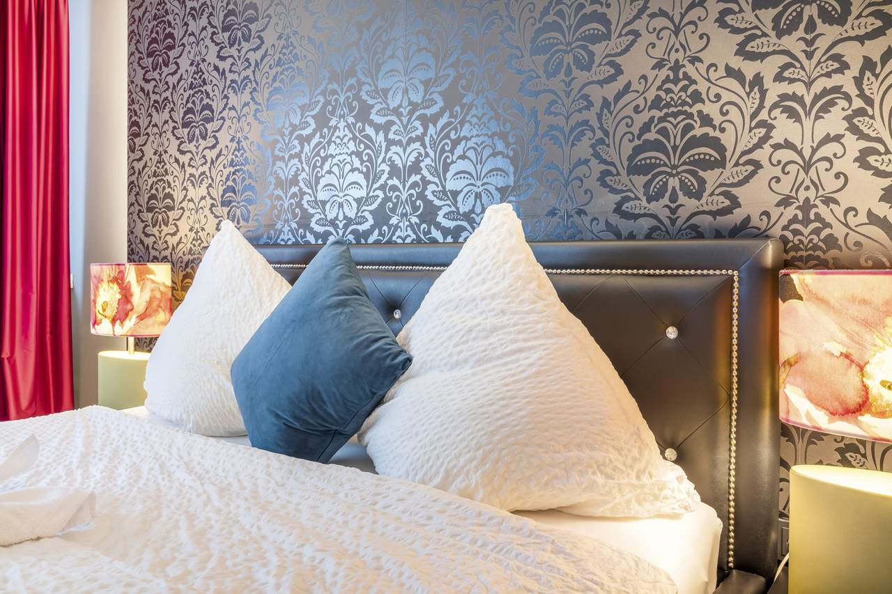 Doppelbett mit weißen Kissen, blauem Kissen und Mustertapete
