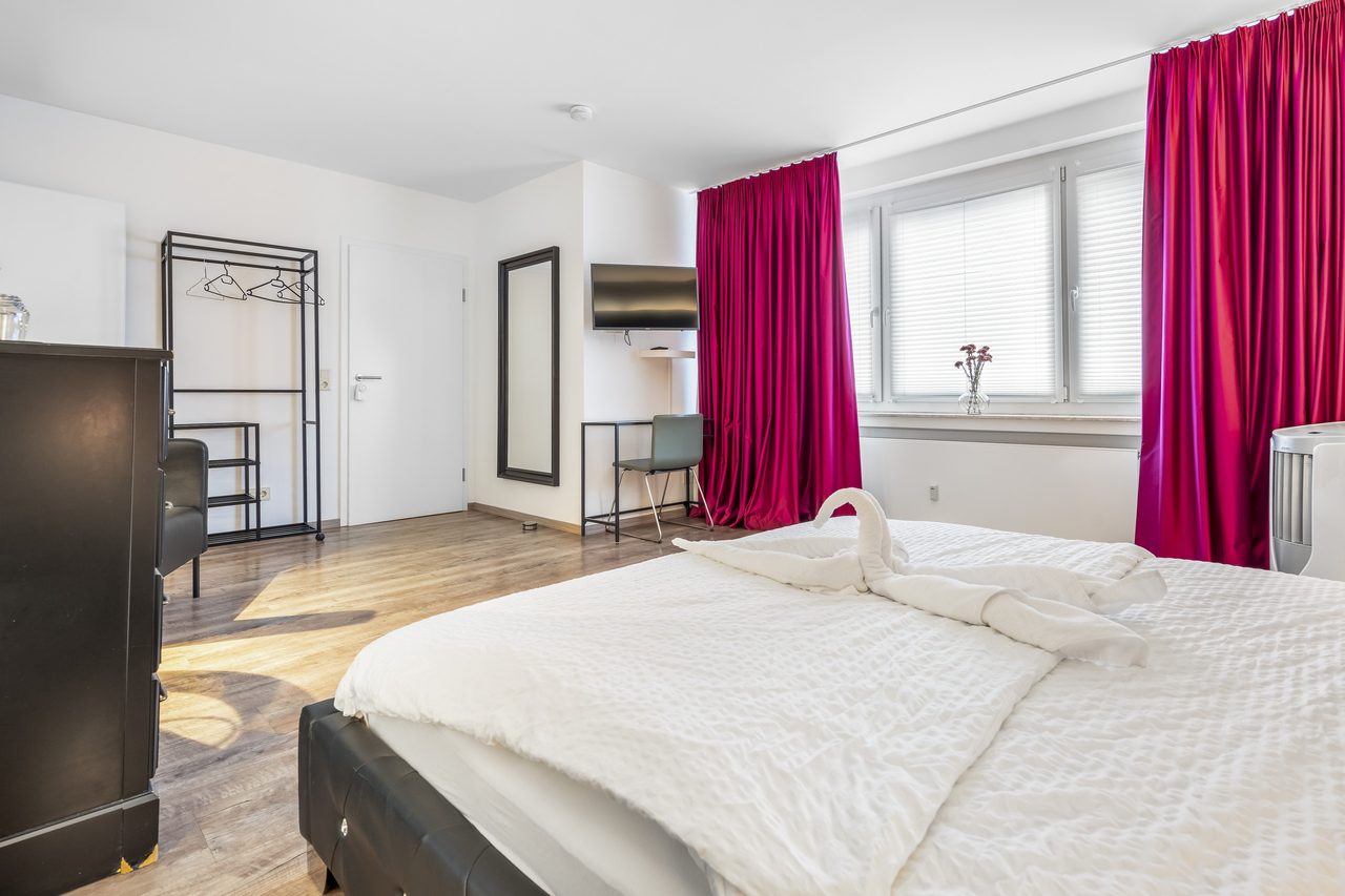 Zimmer mit Bett, Handtuchschwan und pinken Vorhängen