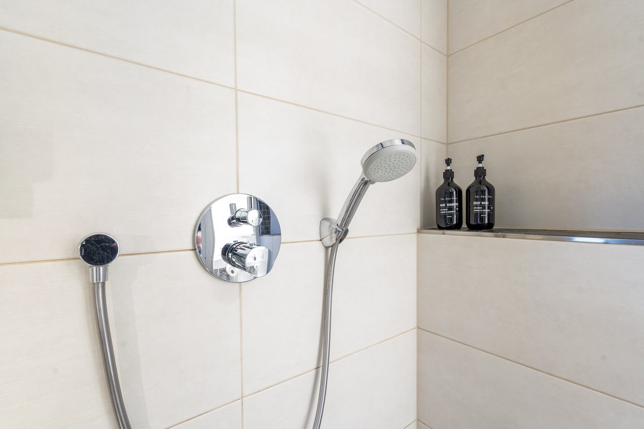 Dusche mit Handbrause, Armatur und zwei Pflegeflaschen