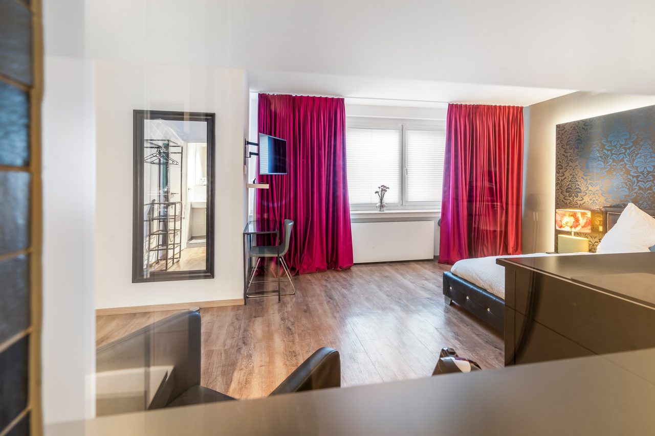 Blick ins Zimmer mit Bett, Spiegel und pinken Vorhängen