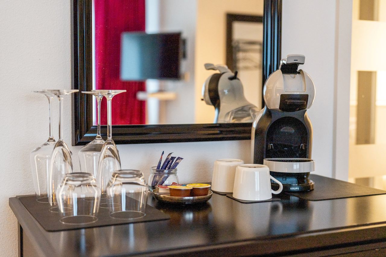 Kommode mit Kaffeekapselmaschine, Gläsern und Tassen vor Spiegel