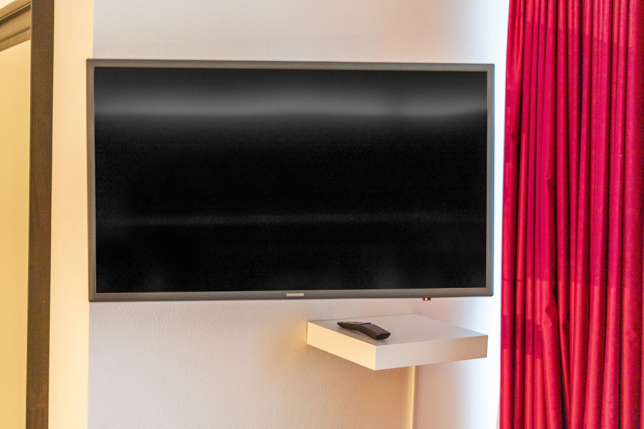 Wandfernseher mit kleiner Ablage neben pinkem Vorhang