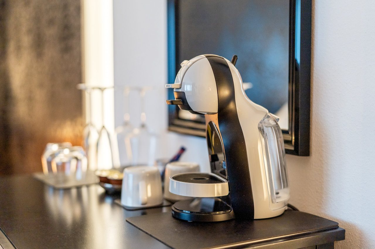 Kaffeekapselmaschine mit Tassen und Gläsern auf dunkler Kommode