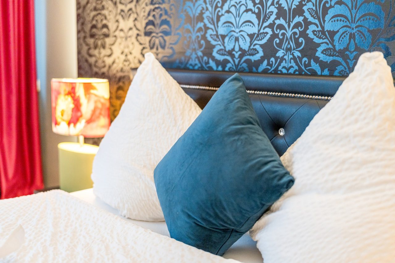 Bett mit weißen Kissen und blauem Kissen vor Mustertapete