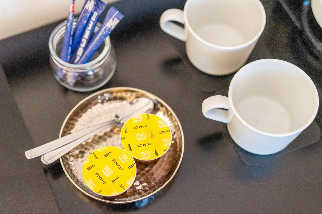 Kaffeekapseln, Löffel und Zucker neben zwei weißen Tassen