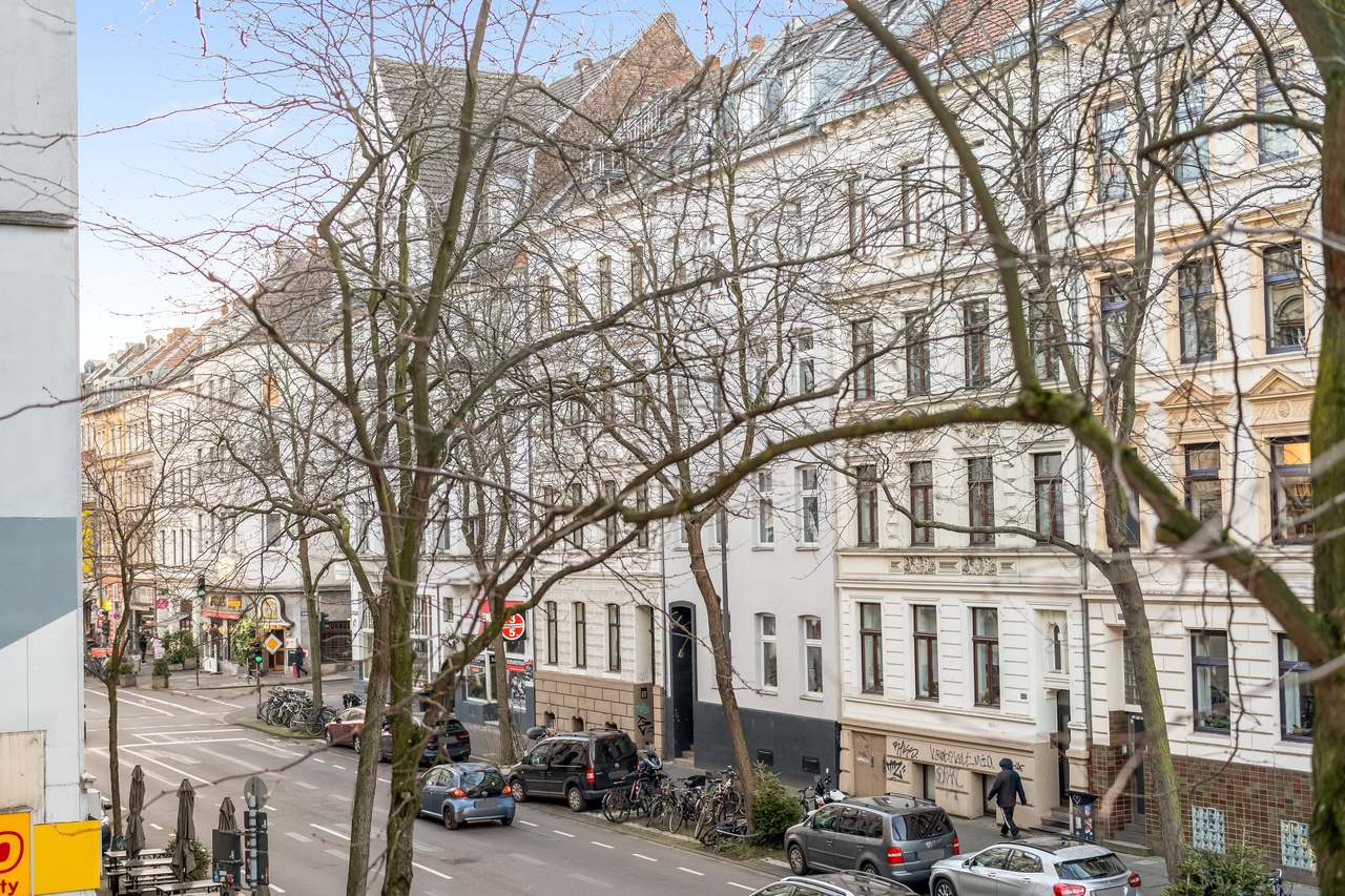 Blick auf Straße mit Altbauten, kahlen Bäumen und parkenden Autos