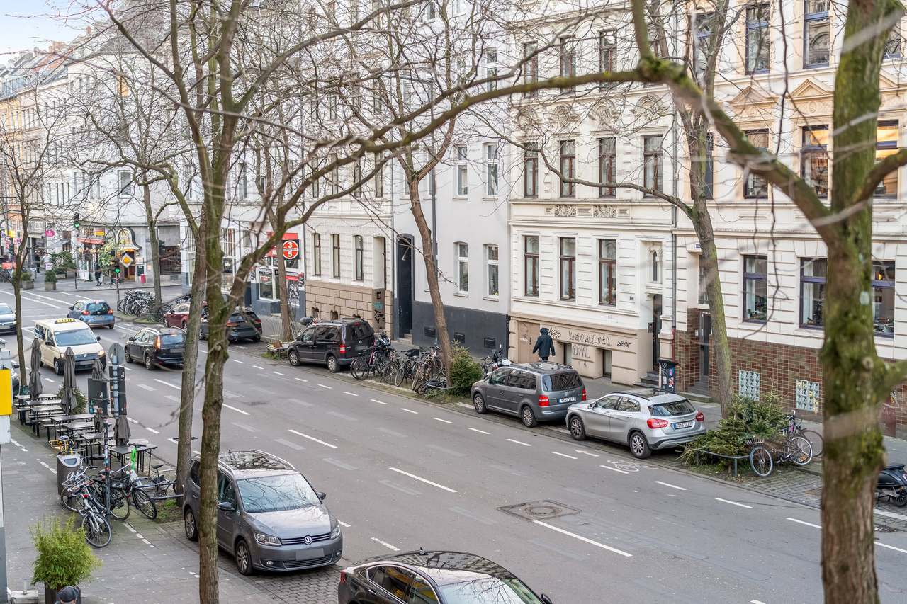 Straße mit Altbaufassaden, kahlen Bäumen und geparkten Autos