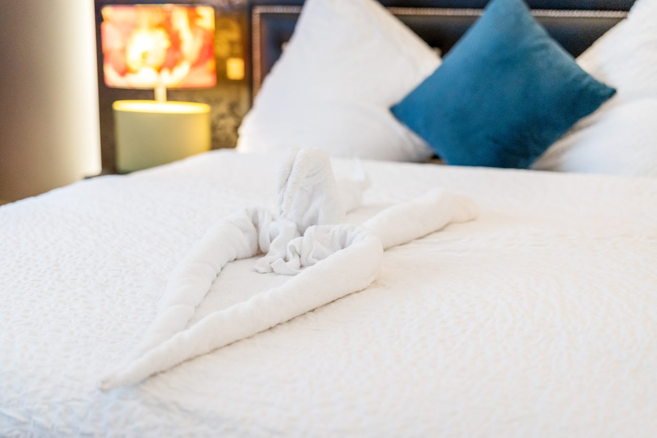 Bett mit Handtuchfigur, weißen Kissen und blauem Kissen