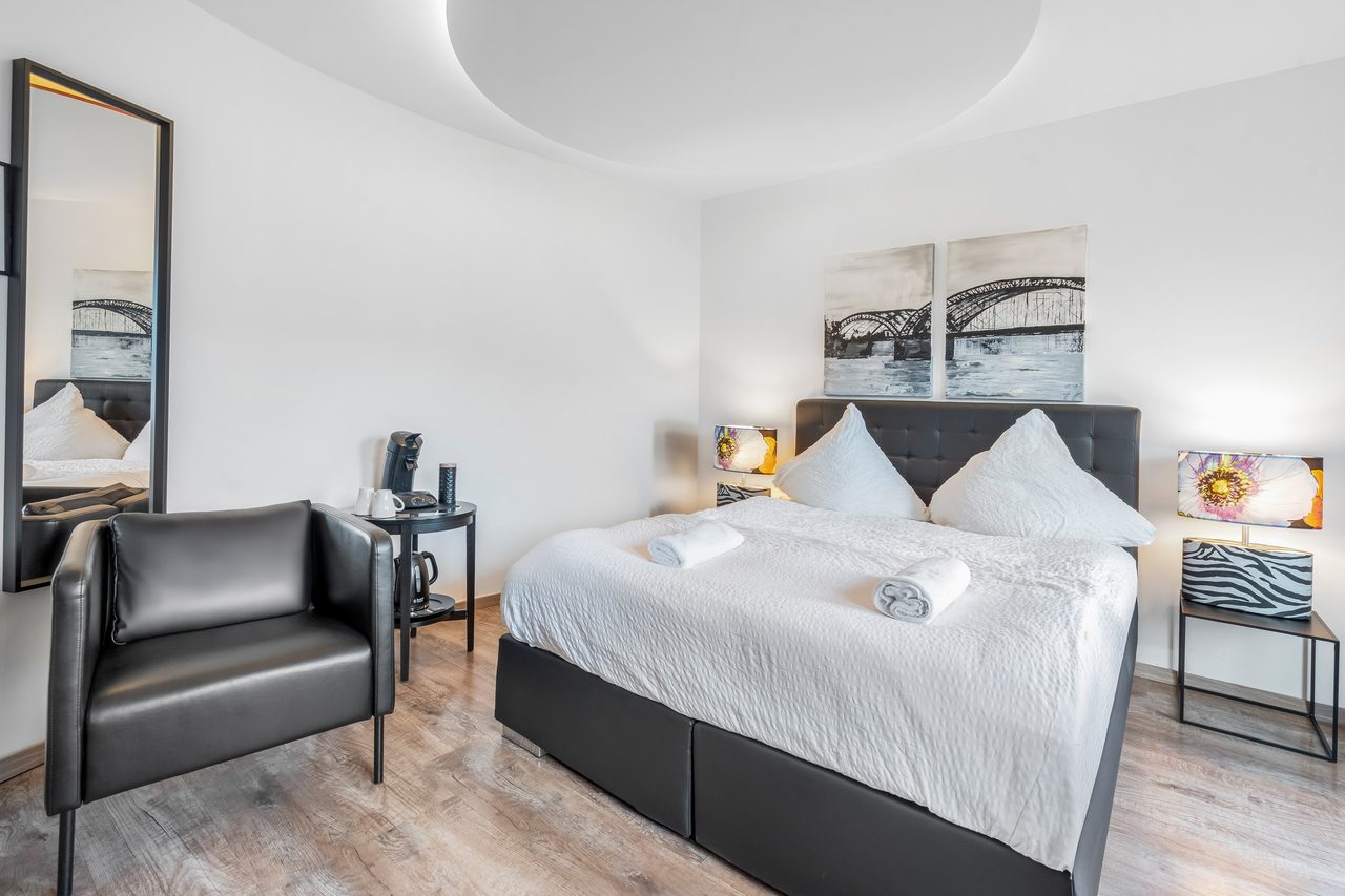 Schlafzimmer mit Boxspringbett, schwarzem Ledersessel und Brückenbild über dem Bett