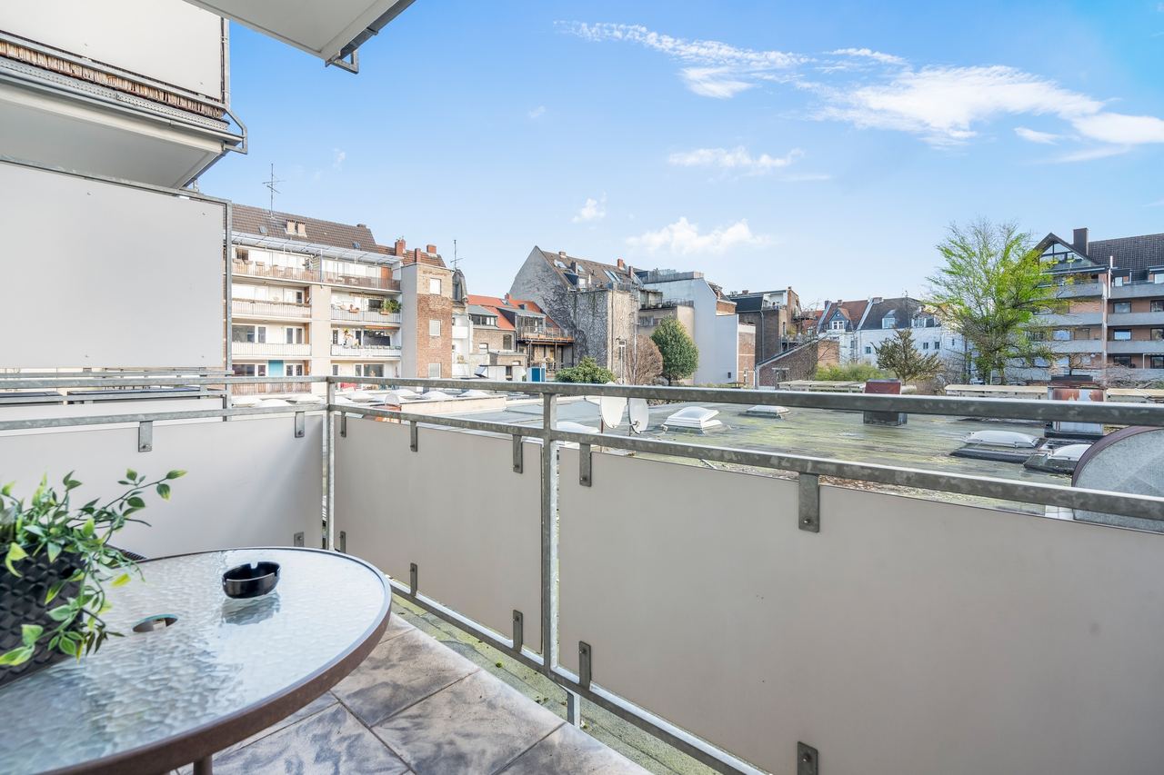 Balkon mit Glastisch, Grünpflanze und Blick auf Häuserreihen