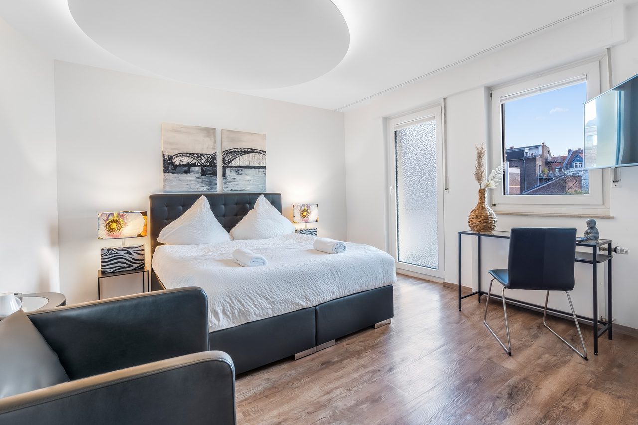 Schlafzimmer mit Doppelbett, Schreibtisch mit Stuhl und Wandfernseher
