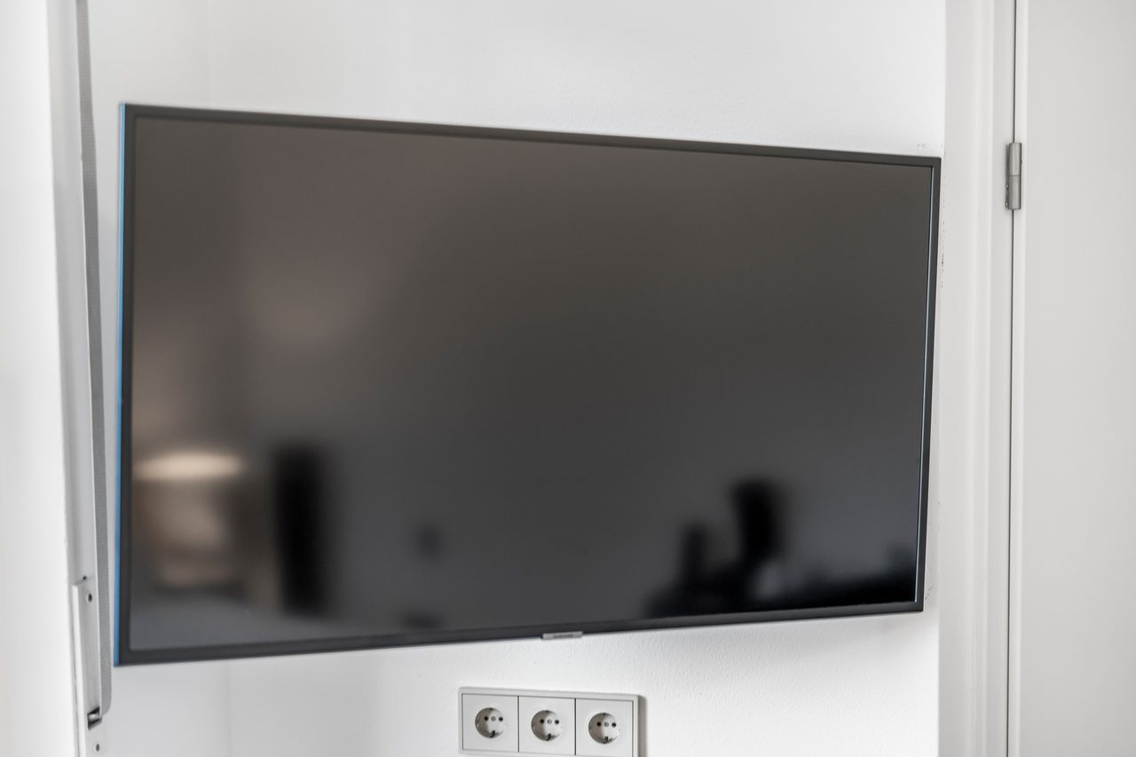 Großer Wandfernseher über Steckdosen an weißer Wand