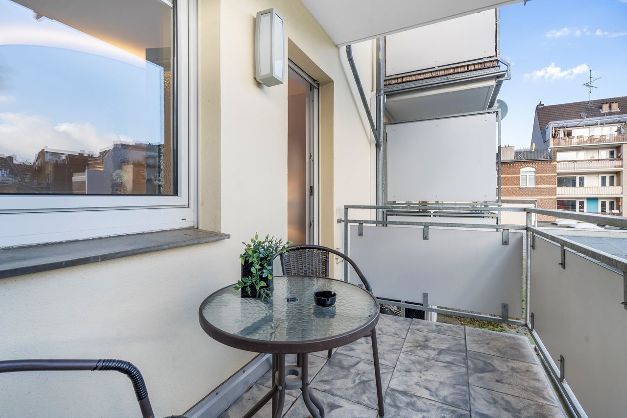 Balkon mit rundem Glastisch, Stühlen und Blick auf Nachbarhäuser