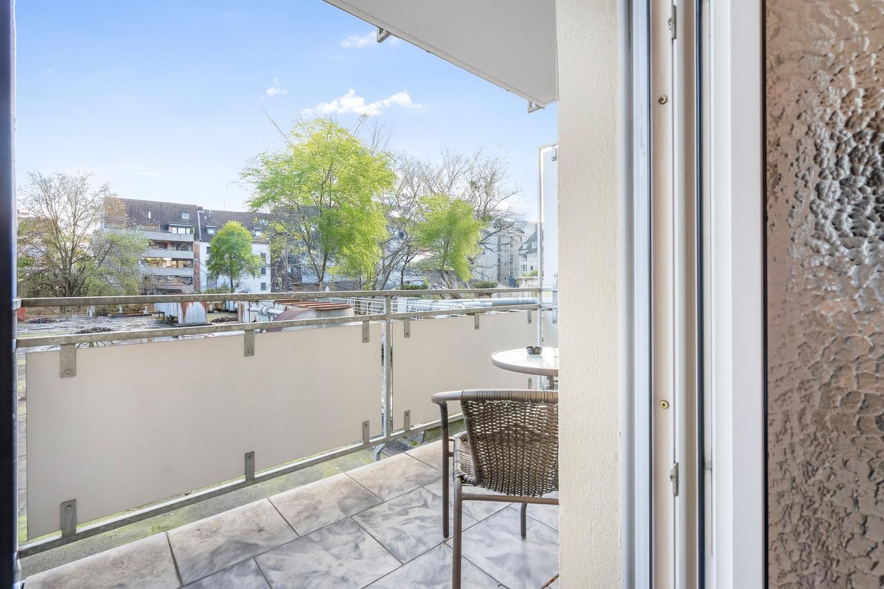 Balkon mit Rattanstuhl, Glastisch und Blick auf Bäume