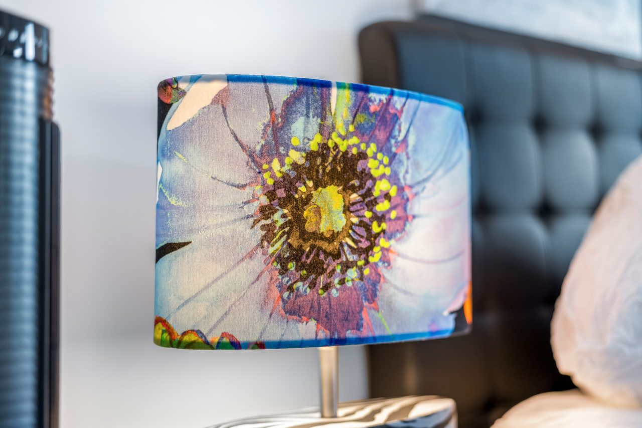 Nachttischlampe mit Blumenmotiv neben schwarzem gepolstertem Kopfteil