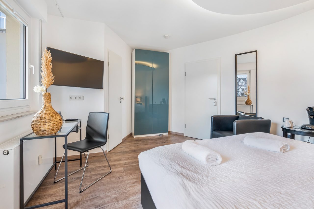 Schlafzimmer mit Bett, Schreibtisch mit Stuhl und Wandfernseher