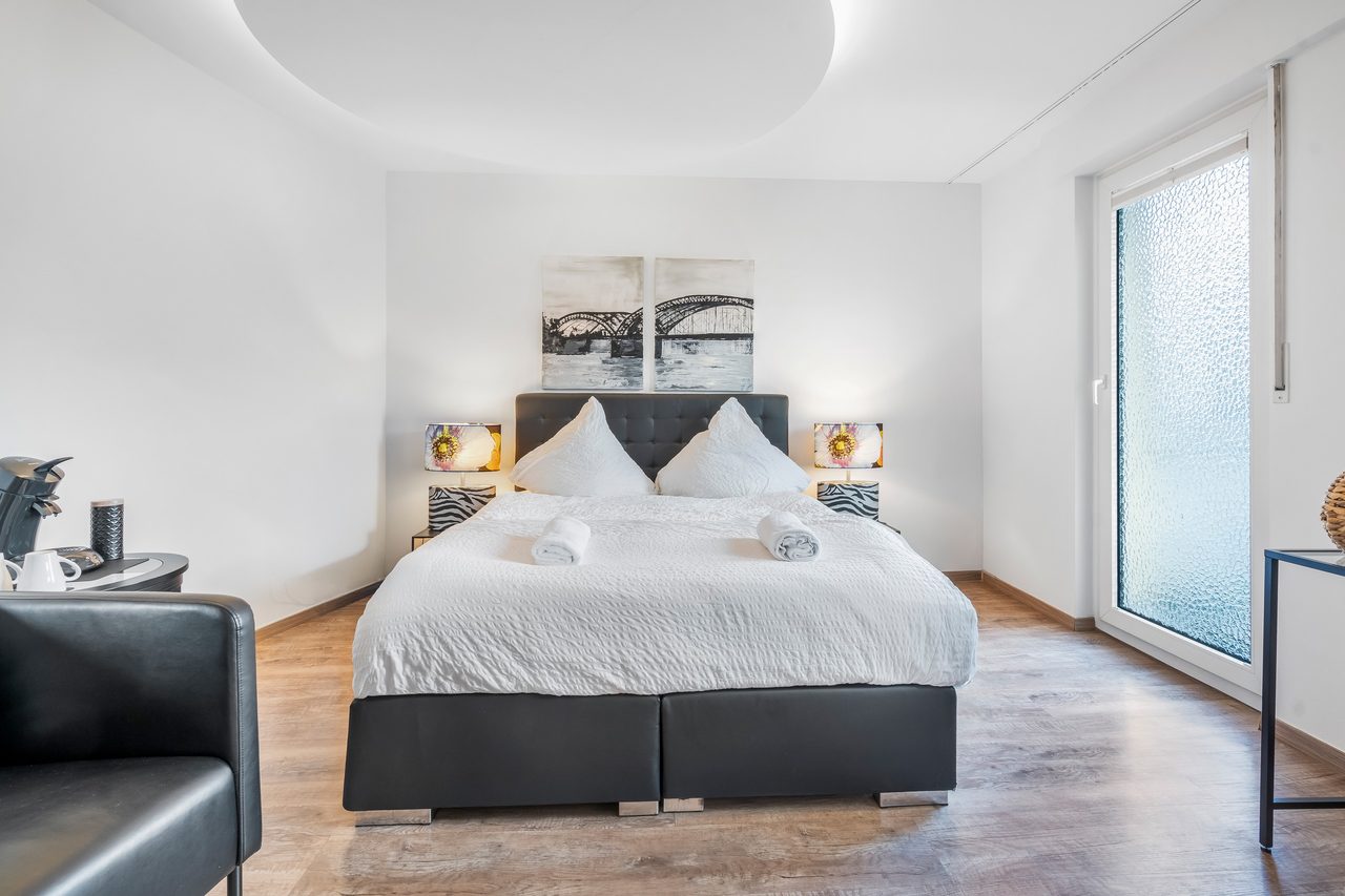 Schlafzimmer mit Boxspringbett, zwei Nachttischlampen und Ledersessel