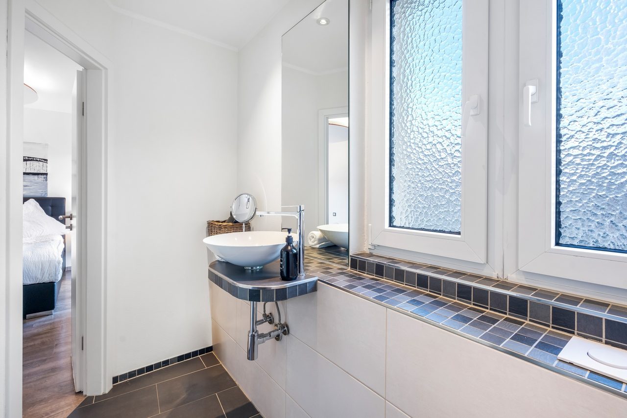 Badezimmer mit Aufsatzwaschbecken, Milchglasfenstern und Blick ins Schlafzimmer
