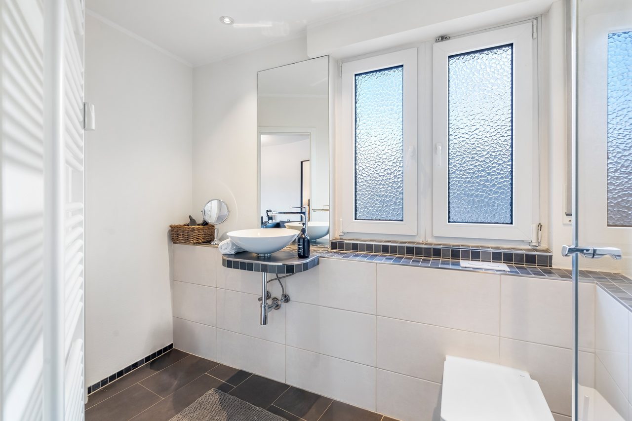 Badezimmer mit Aufsatzwaschbecken, Spiegel und zwei Milchglasfenstern