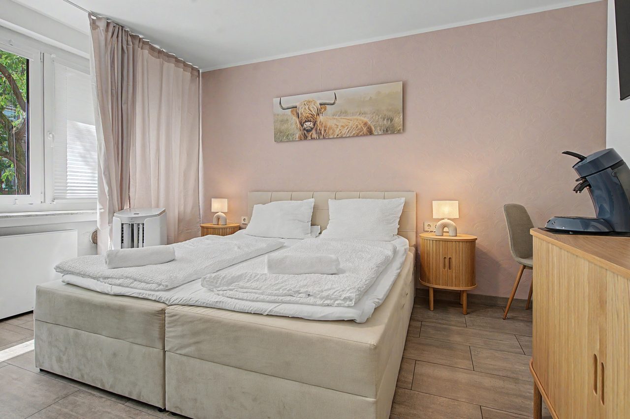 Schlafzimmer mit Doppelbett, Holzsideboard und Bild mit Hochlandrind