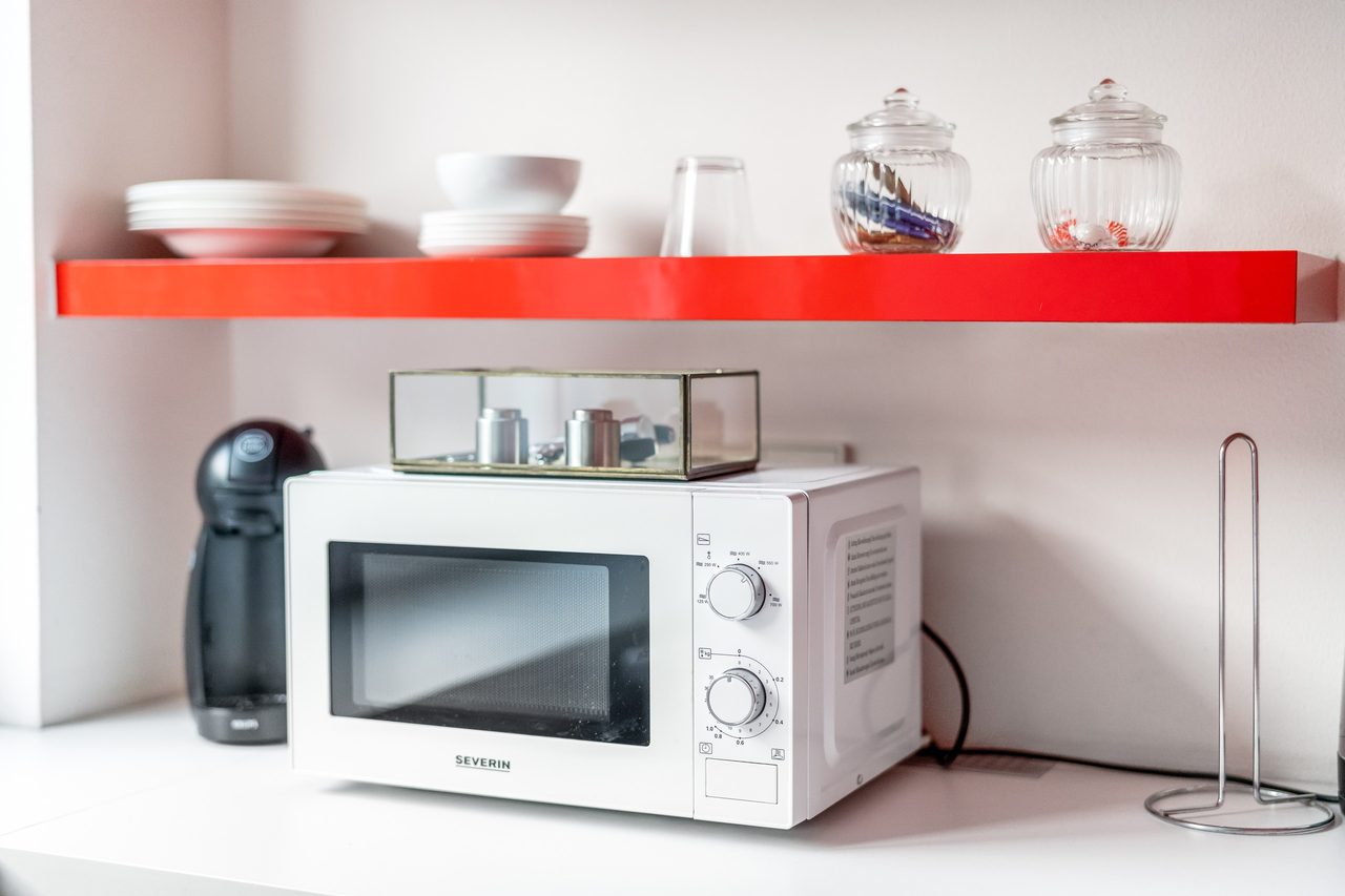 Rotes Wandregal mit Geschirr über Mikrowelle und Kaffeemaschine