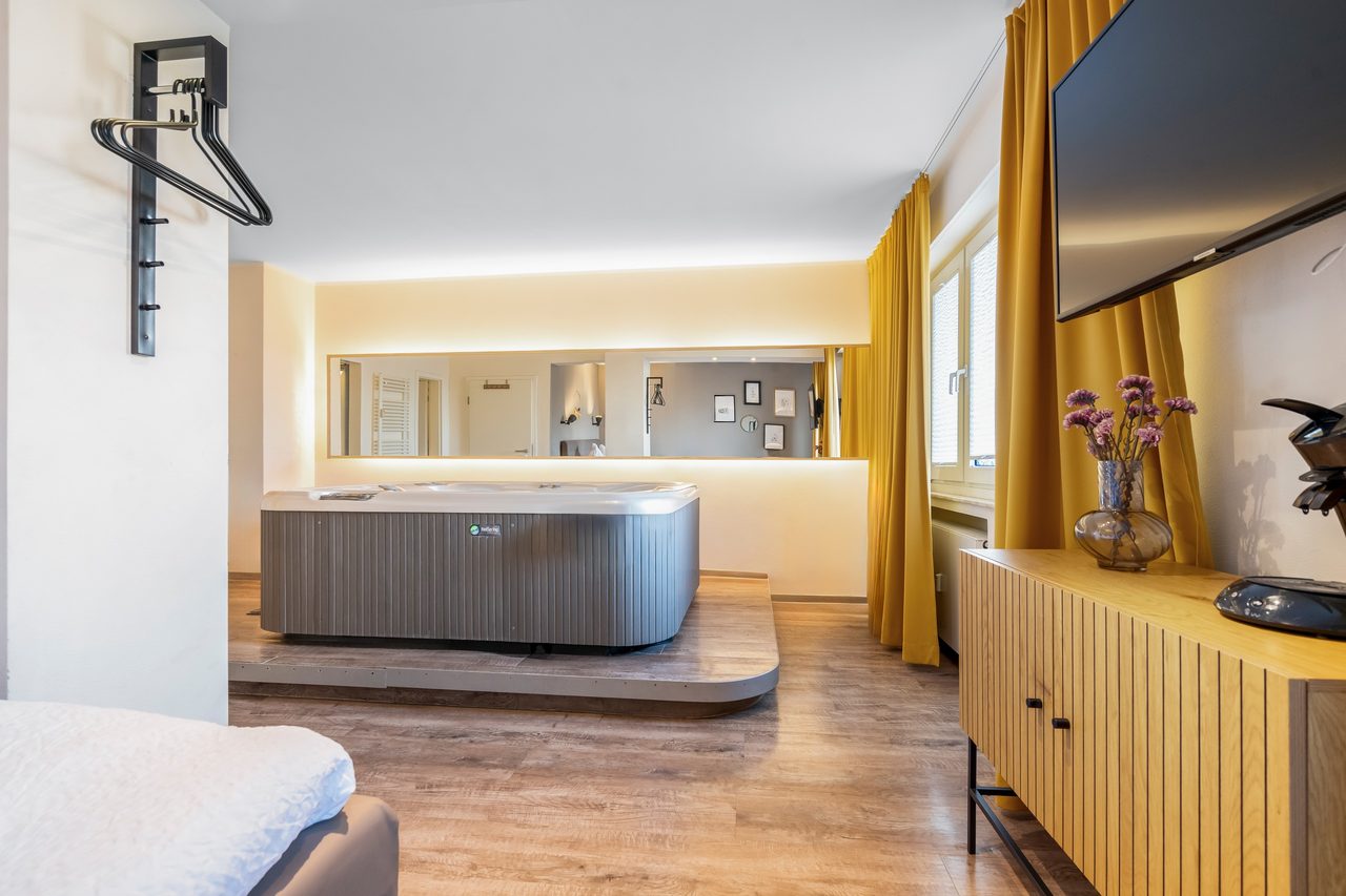 Zimmer mit Whirlpool auf Podest, Wandfernseher und Sideboard