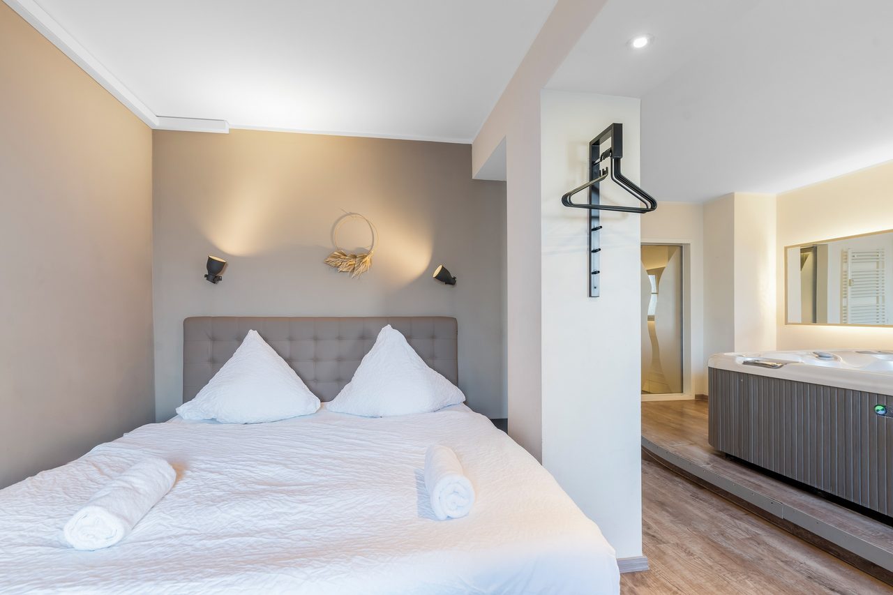 Schlafzimmer mit Doppelbett, Wandgarderobe und Whirlpool im Hintergrund