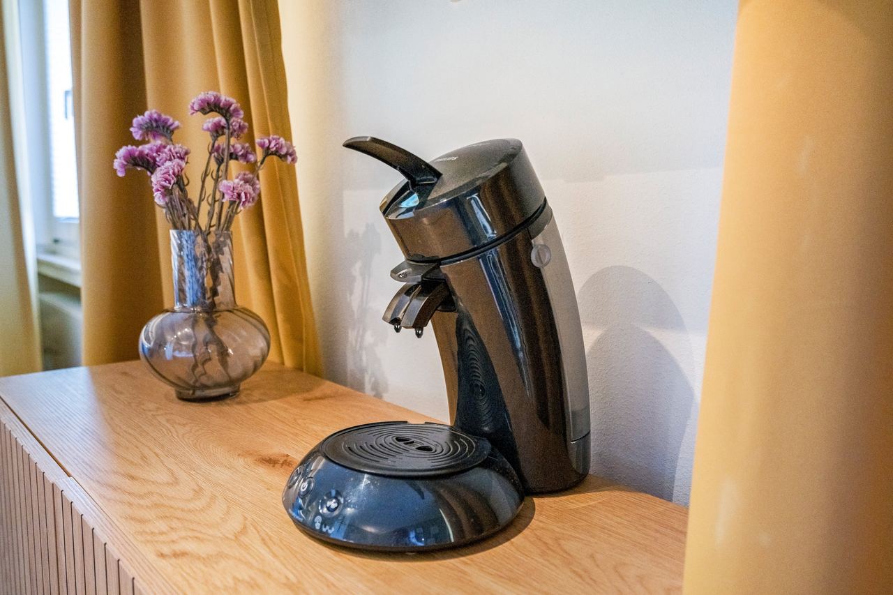 Kaffeepadmaschine und Vase mit lila Blumen auf Holzmöbel