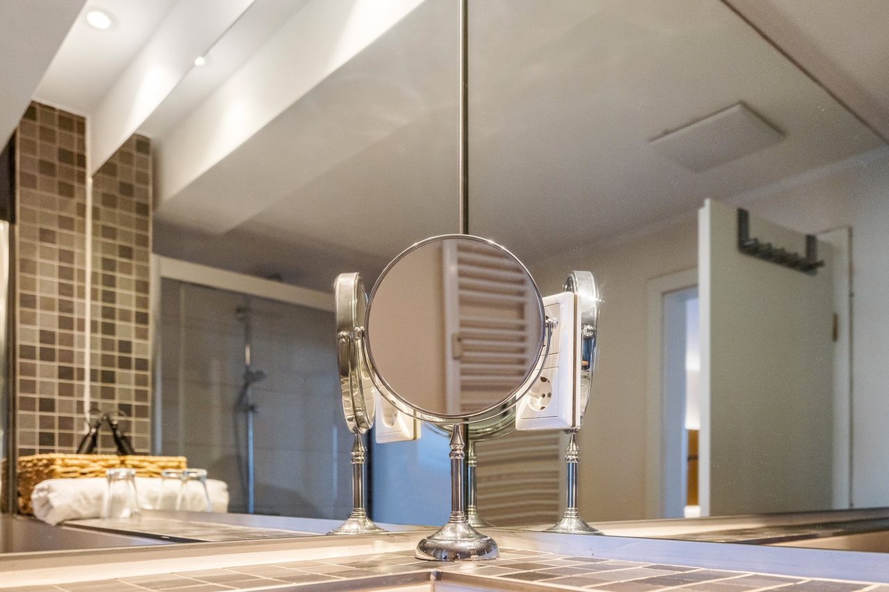Badezimmer mit Kosmetikspiegel, Mosaikfliesen und Glasdusche im Hintergrund