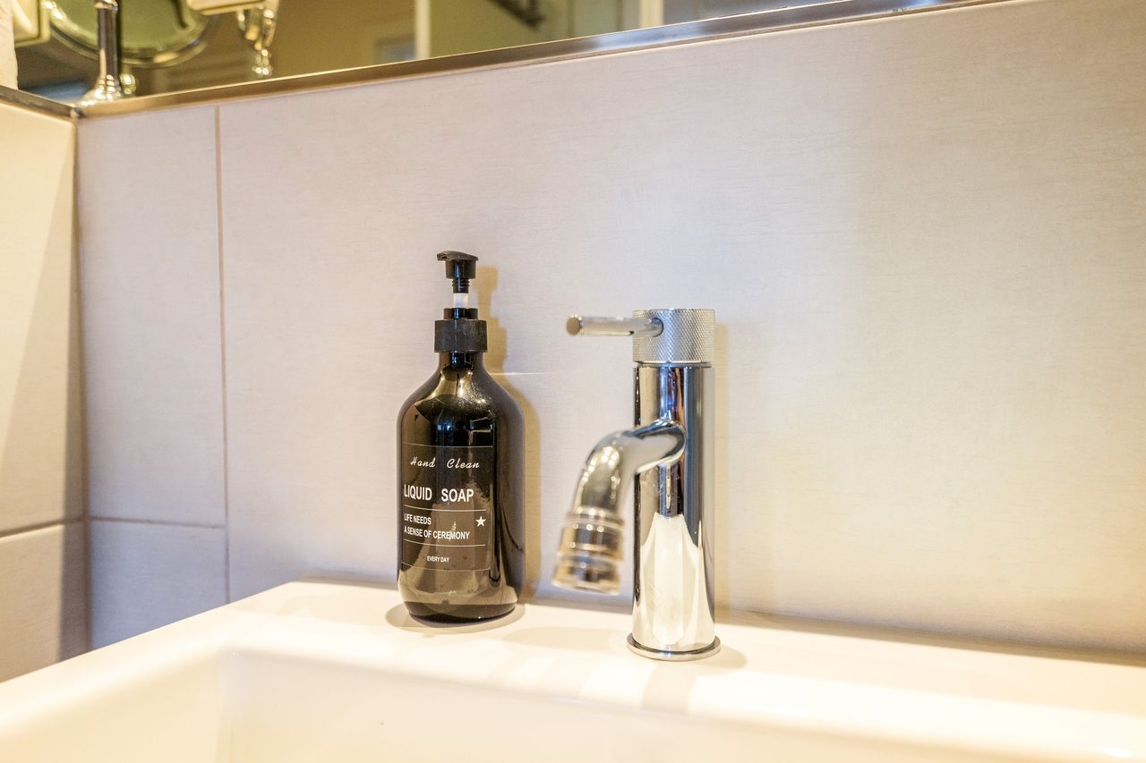 Waschbecken mit Chromarmatur und Seifenspender aus dunklem Glas