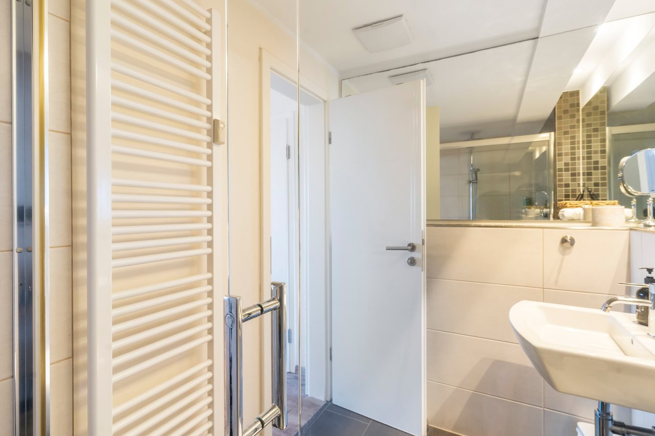 Badezimmer mit Handtuchheizkörper, Waschbecken und offener Tür