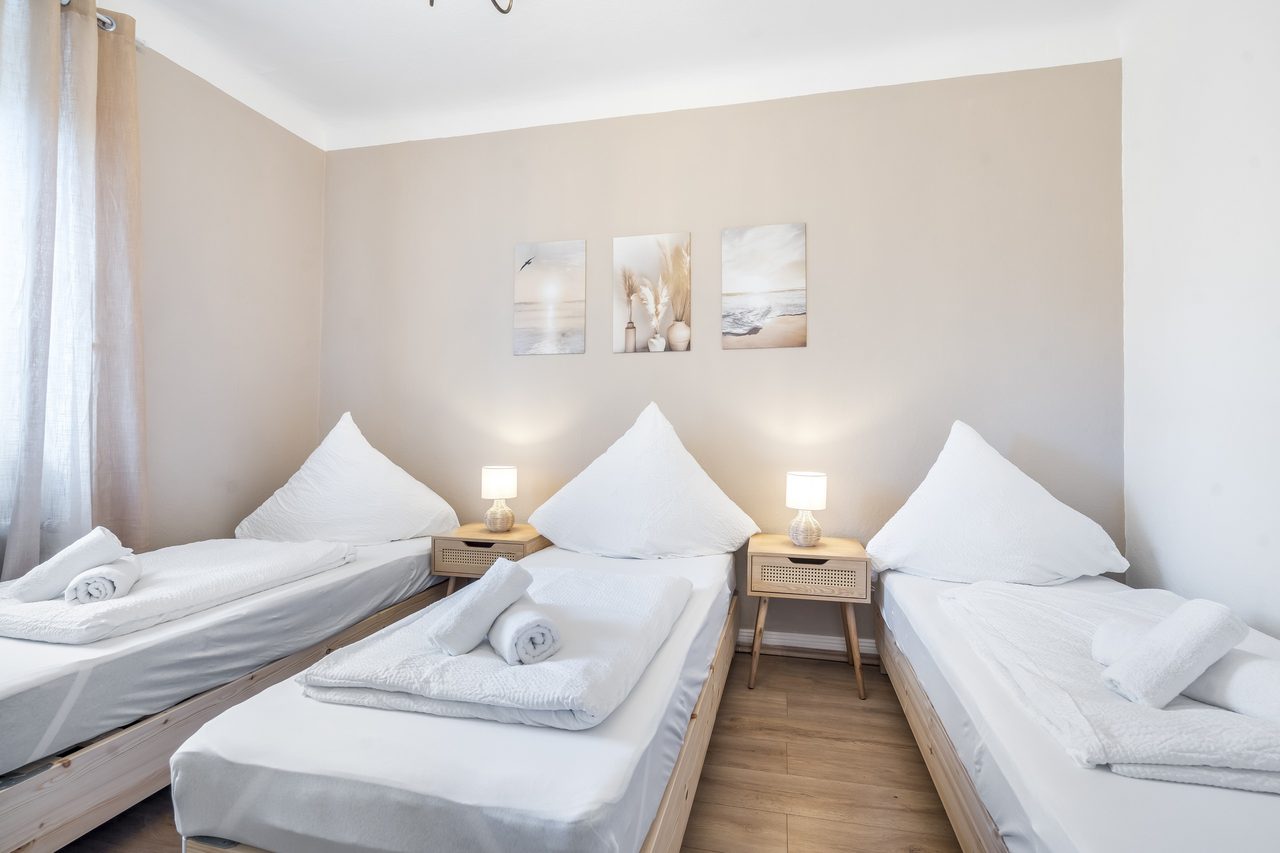 Schlafzimmer mit drei Einzelbetten, Nachttischlampen und Wandbildern