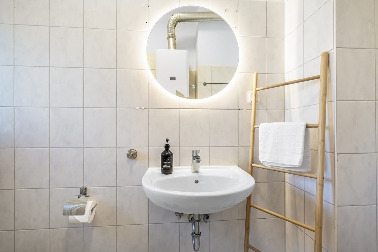 Badezimmer mit Waschbecken, rundem Spiegel und Handtuchleiter