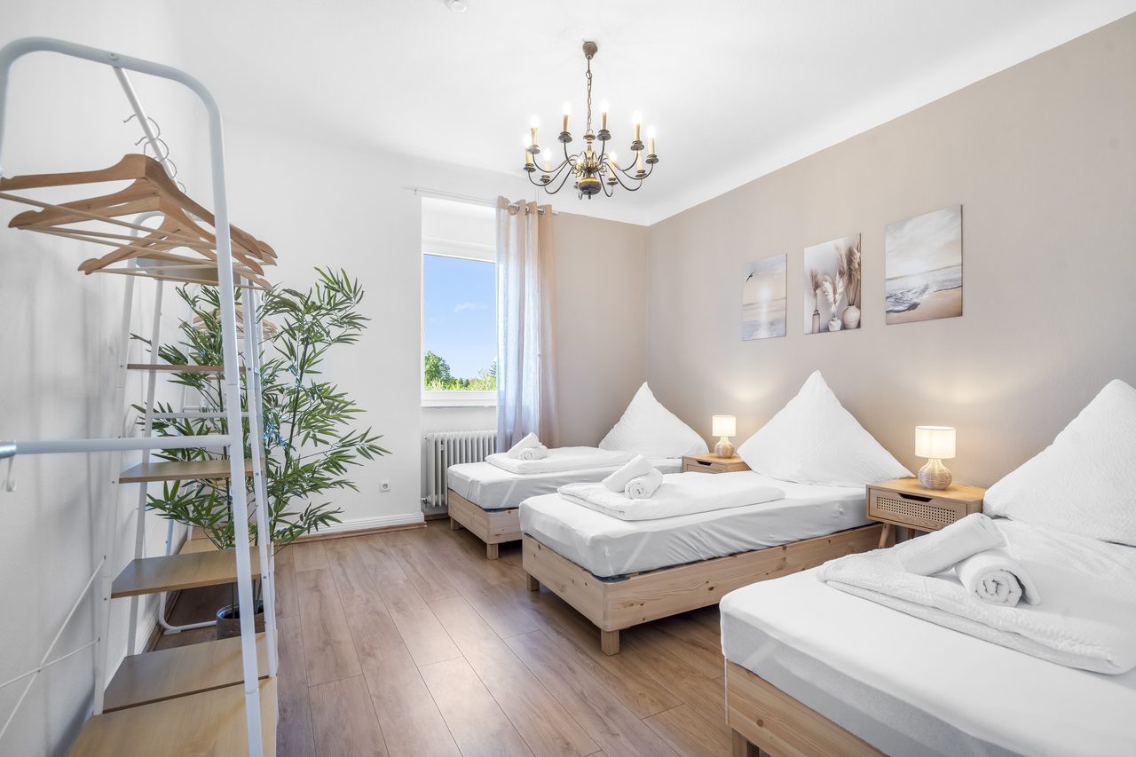 Schlafzimmer mit drei Einzelbetten, Kronleuchter und Kleiderregal