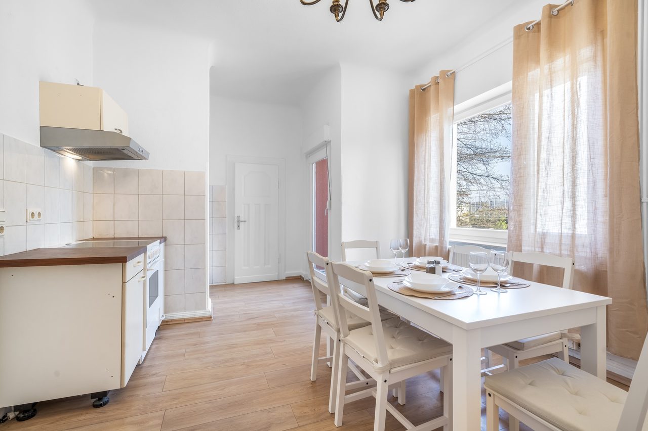 Küche mit Esstisch, weißen Stühlen und Fenster mit Vorhängen