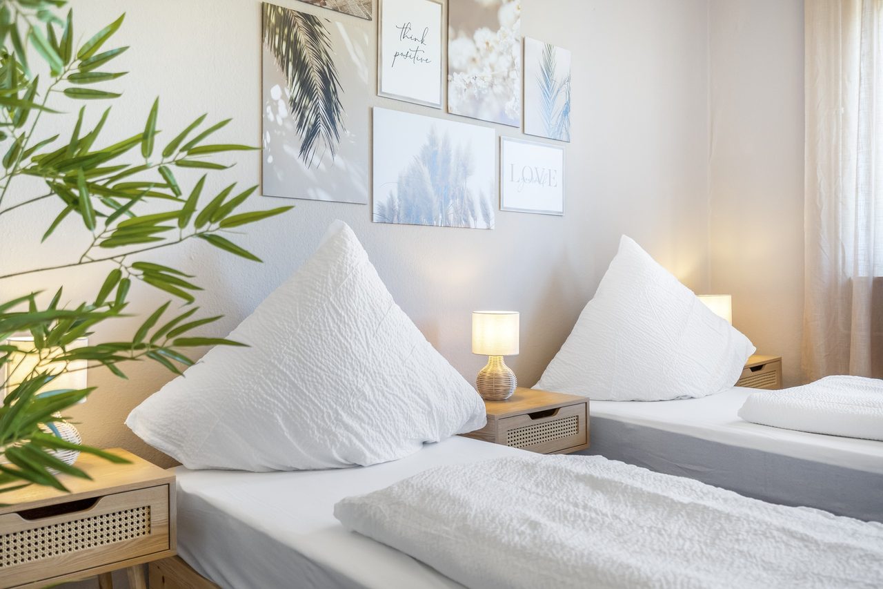 Schlafzimmer mit Einzelbetten, Nachttischlampe und Bilderwand