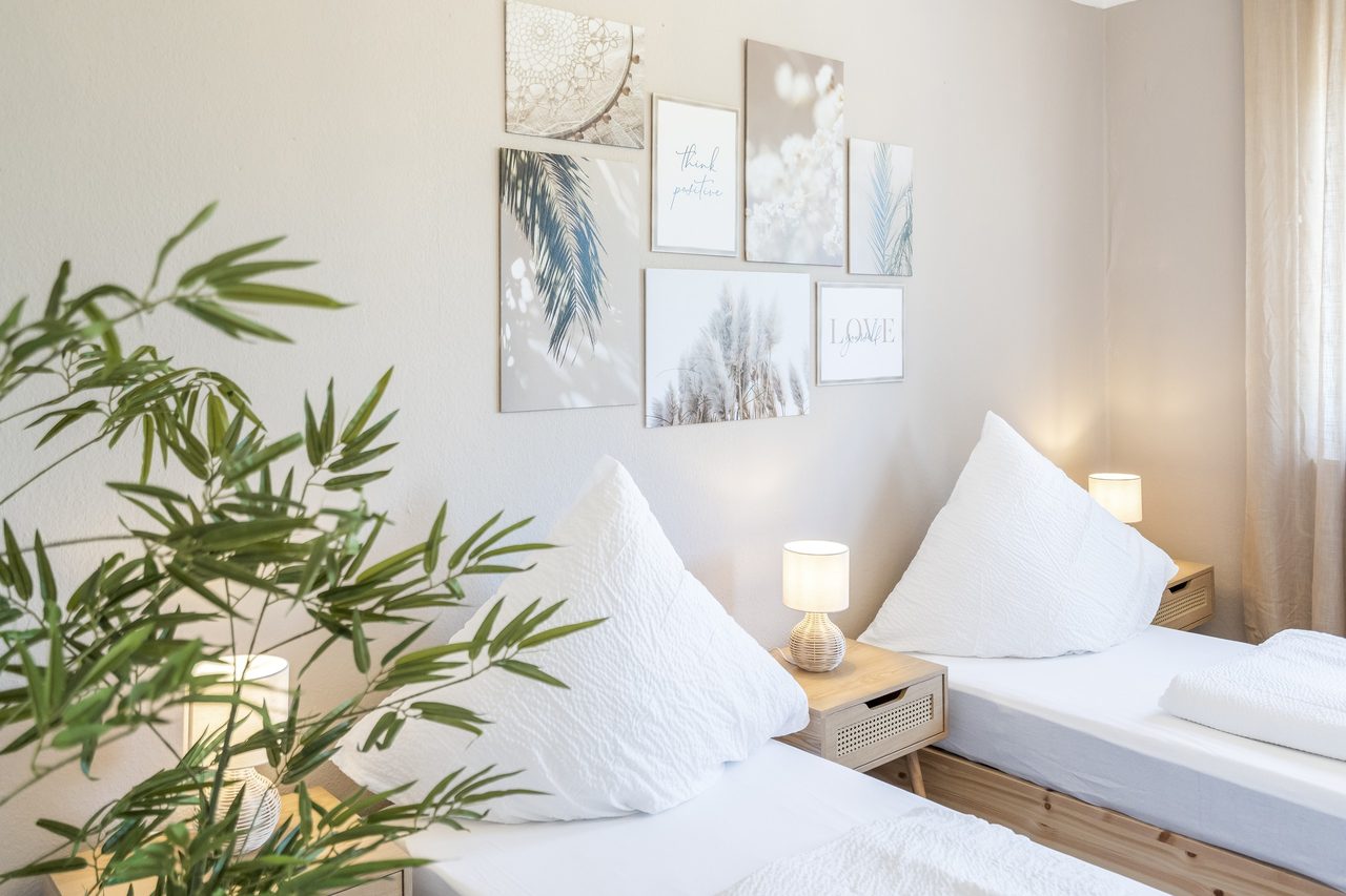 Schlafzimmer mit zwei Einzelbetten, Bilderwand und Bambuspflanze