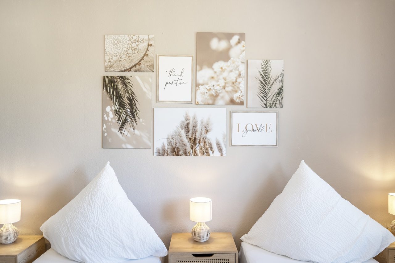 Schlafzimmer mit weißen Kissen, Nachttischlampe und Bildercollage an der Wand