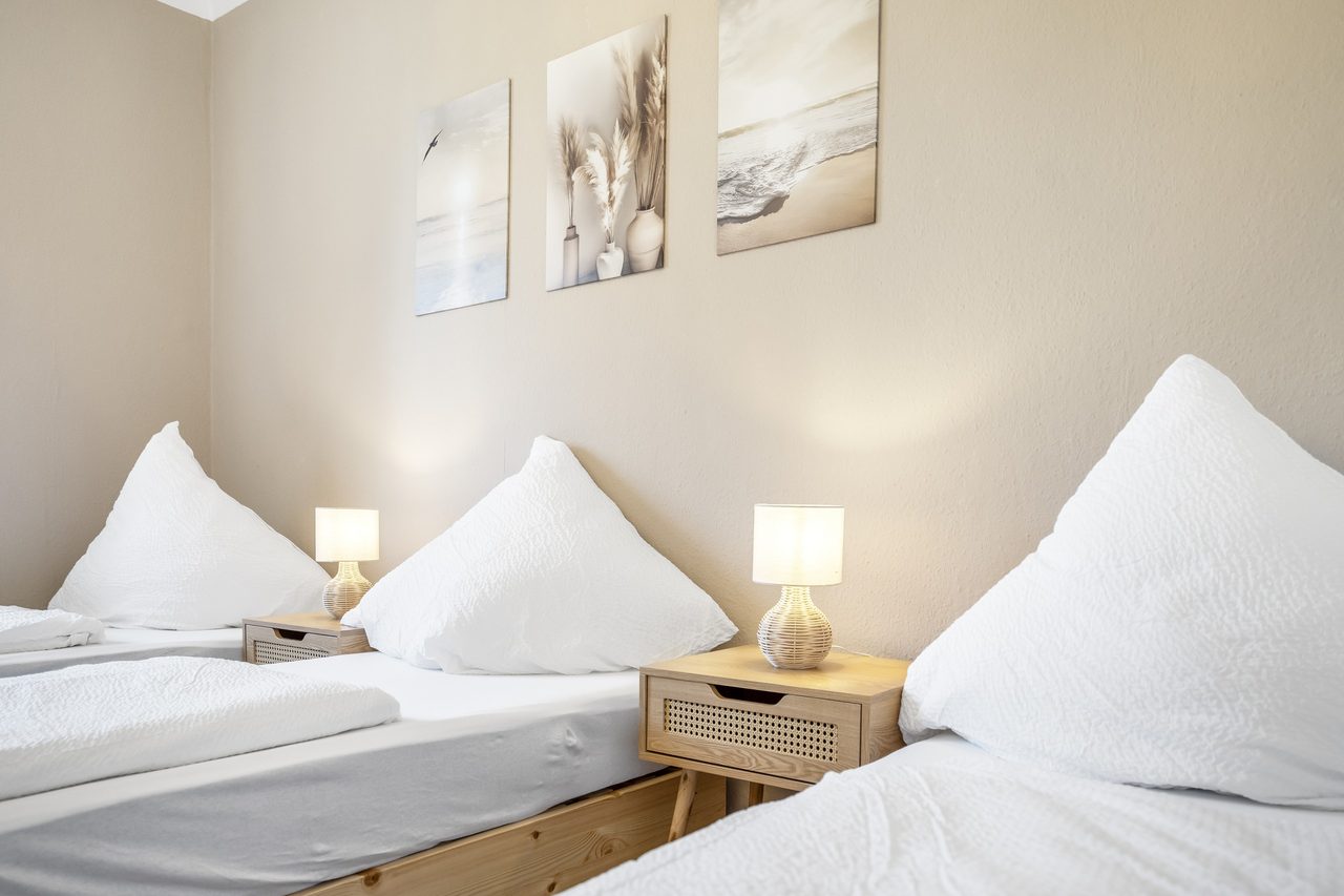 Schlafzimmer mit zwei Einzelbetten, Nachttisch mit Lampe und drei Wandbildern