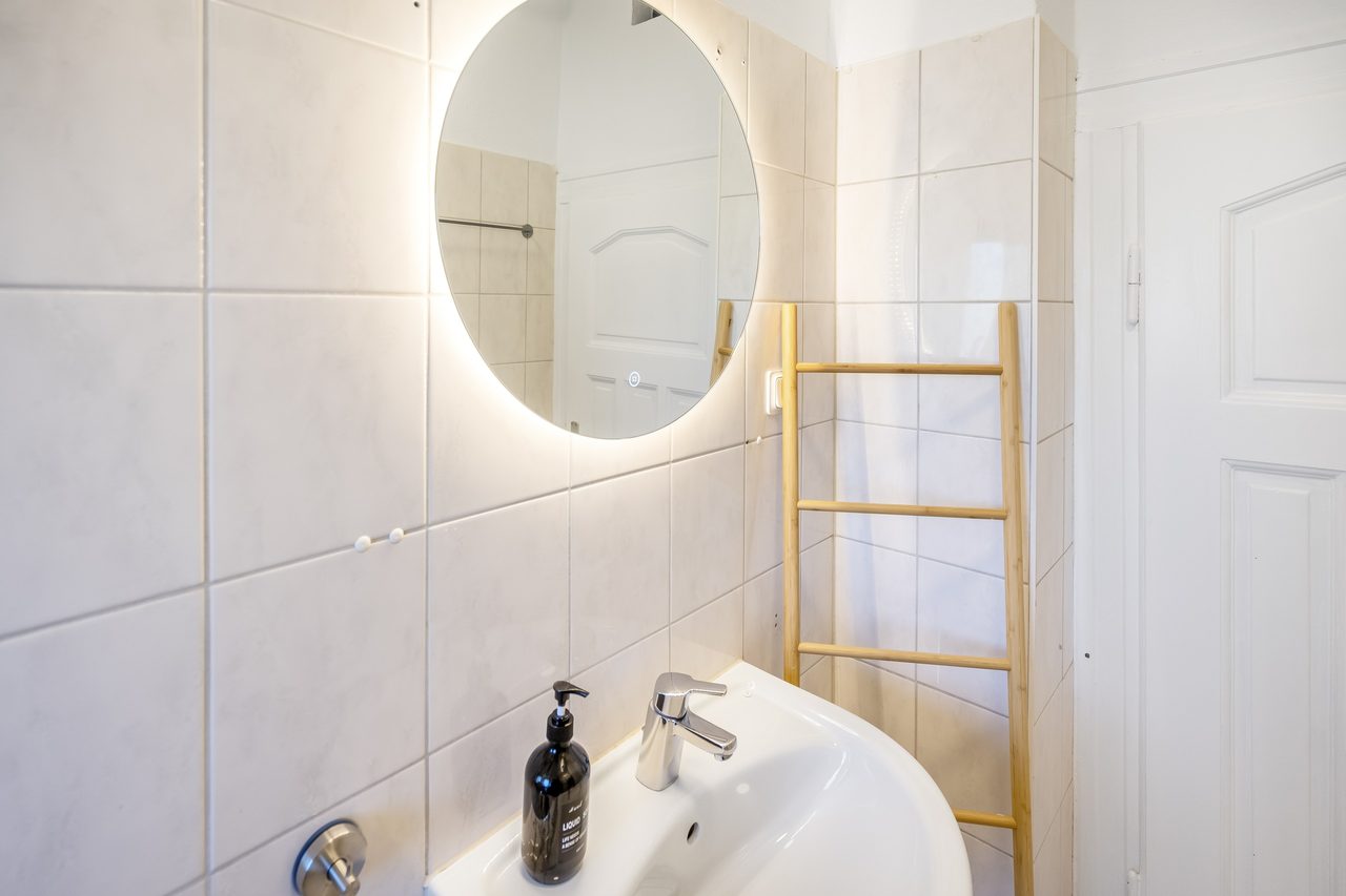 Badezimmer mit rundem beleuchtetem Spiegel, Waschbecken und Handtuchleiter aus Holz