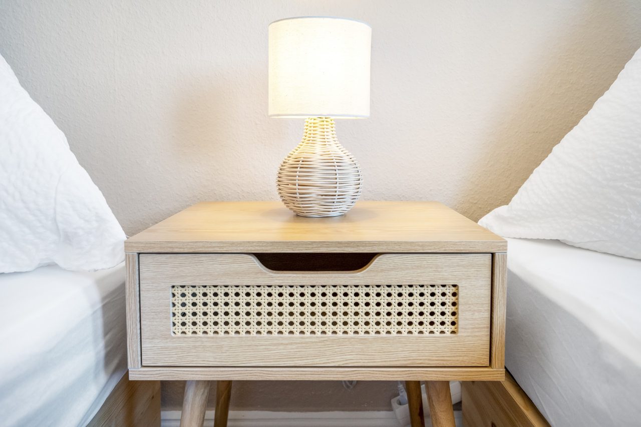Nachttisch aus Holz mit Rattanfront und Tischlampe zwischen zwei Betten