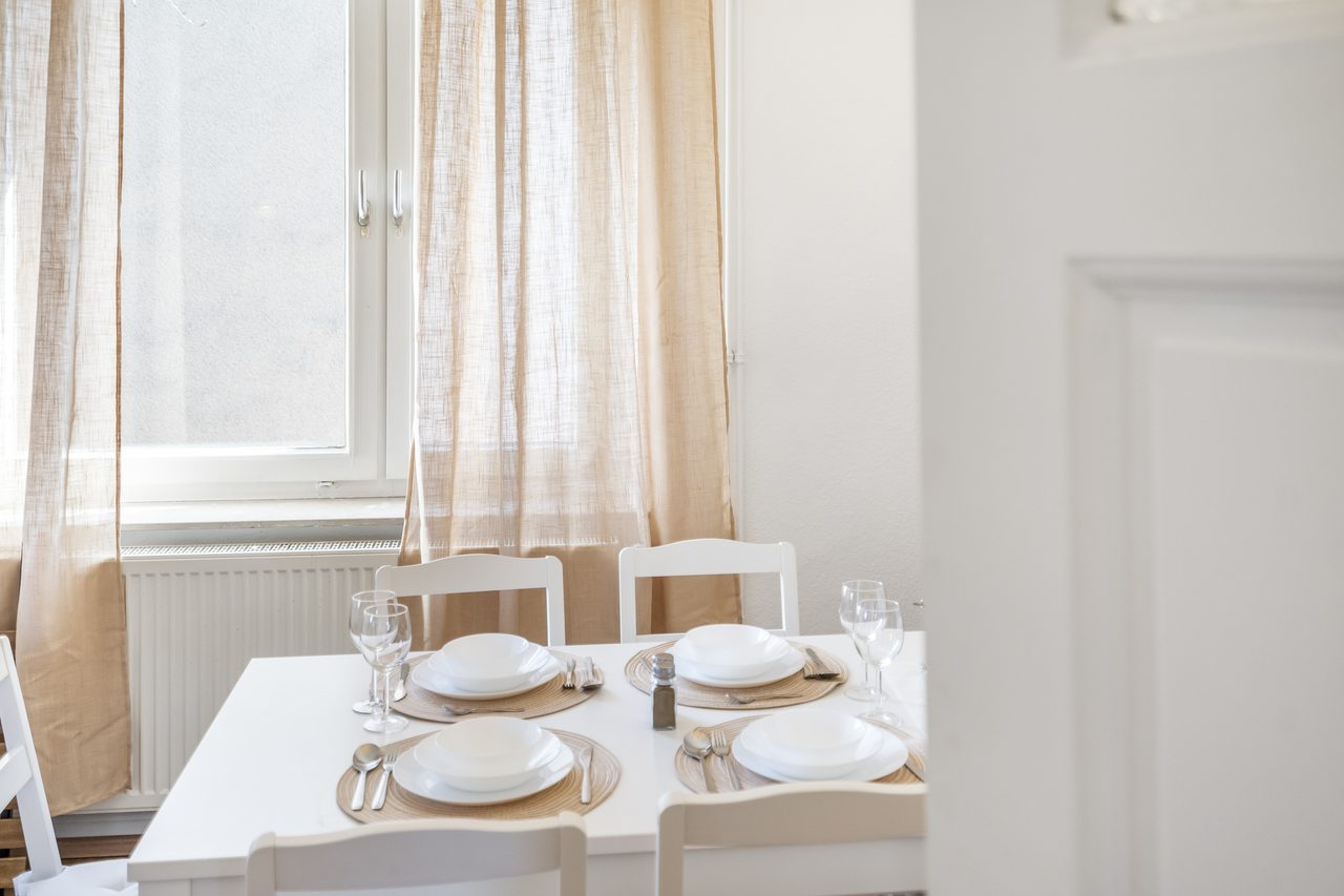 Gedeckter Esstisch mit weißen Tellern und Gläsern vor einem Fenster