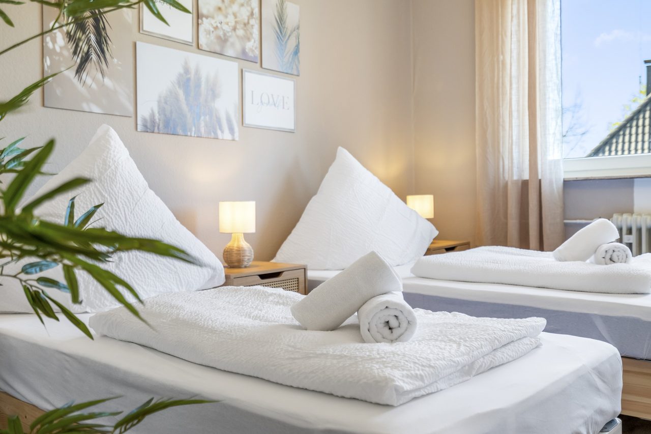 Schlafzimmer mit Einzelbetten, gerollten Handtüchern und Nachttischlampe