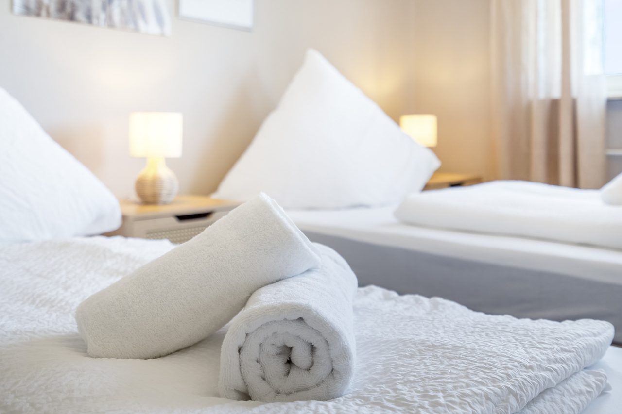Gerollte weiße Handtücher auf einem Bett mit weißer Bettwäsche