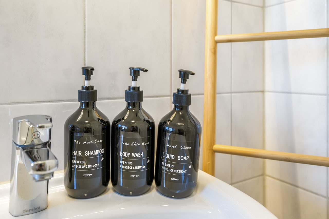 Waschbecken mit Armatur und drei Spenderflaschen für Shampoo, Duschgel und Seife